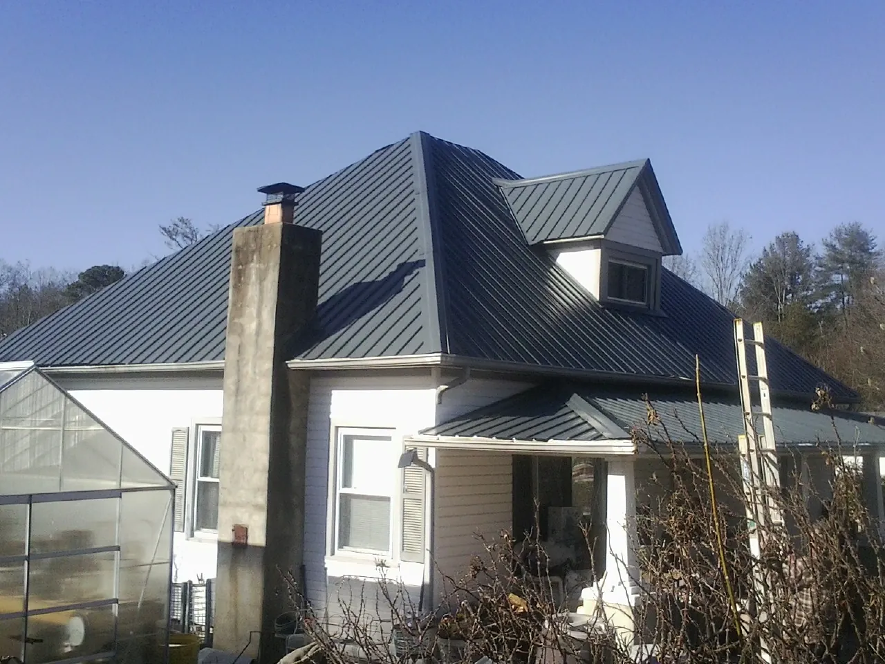 Dark blue standing seam metal roof on a white farmhouse with dormer — Slate & Tile Roof Repair by Roofing Brothers in Middleville