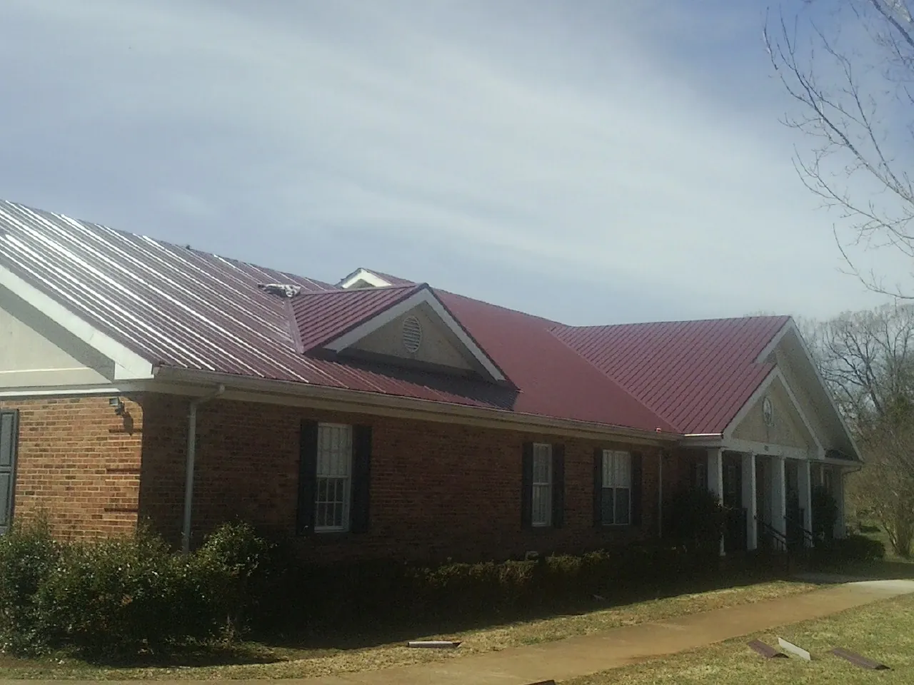 Red metal roof with gabled entries on a long brick building, from a Hail Damage Roof Repair job in Middleville