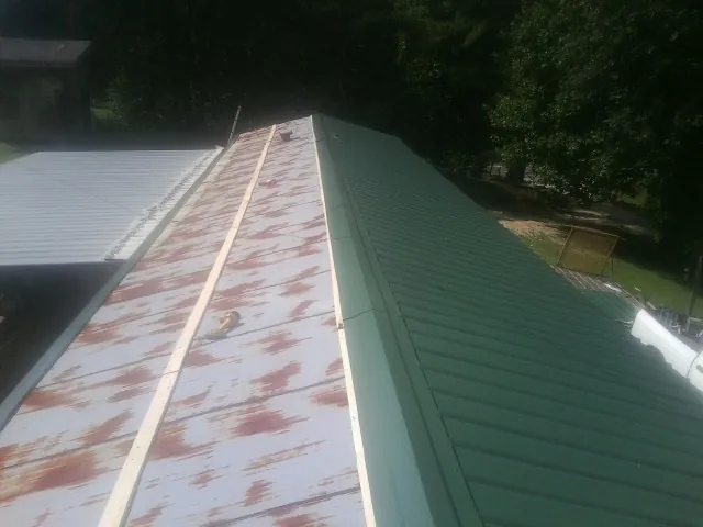 Old rusted panels beside newly installed green metal roofing — Wind Damage Roof Repair by Roofing Brothers in Middleville