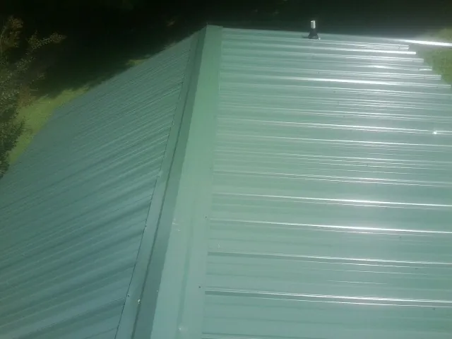 New green metal panels meeting at the ridge of a roof — Flat Roof Repair work by our crew in Middleville