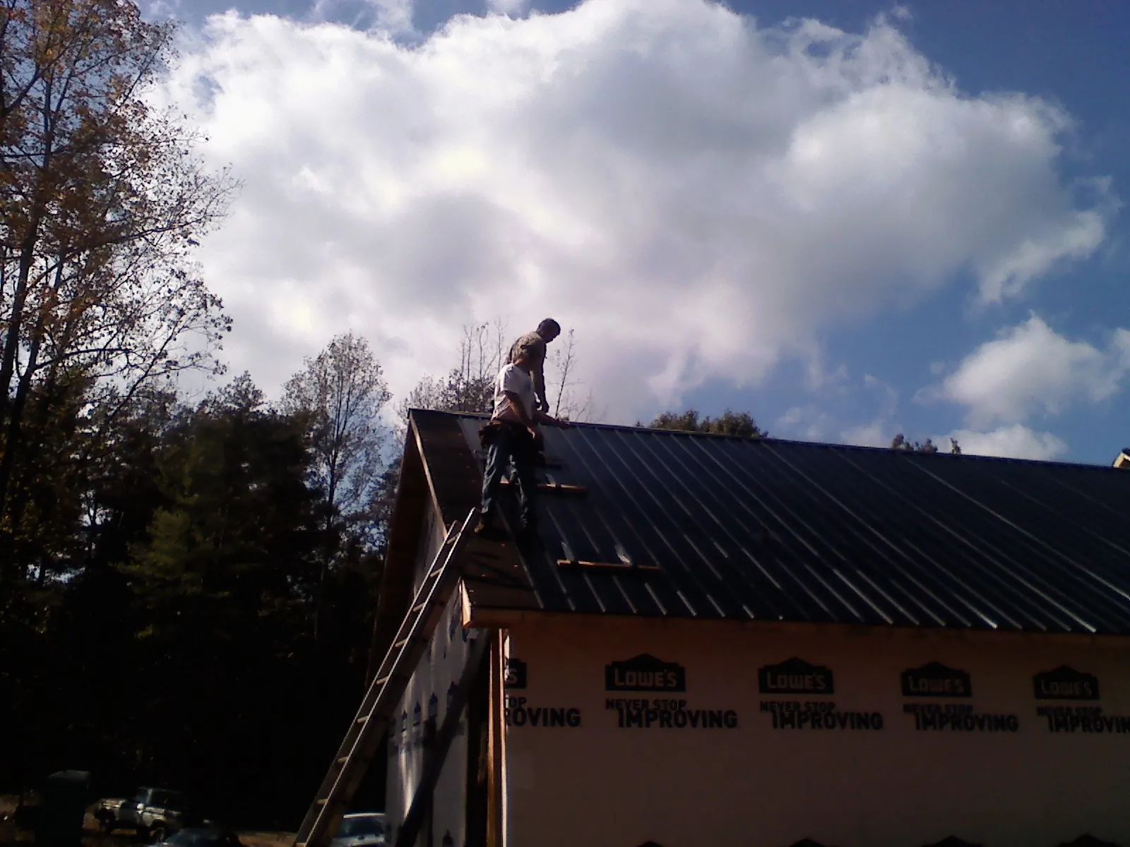 Roofer fastening dark metal panels high against a cloudy sky, from a Roof Inspection job in Middleville