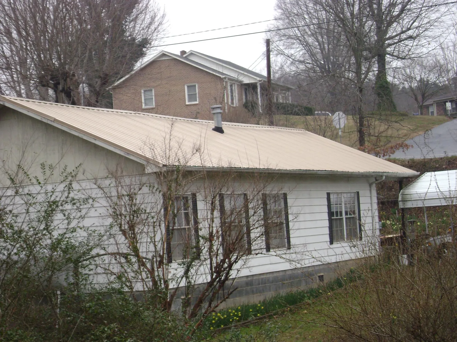 Tan metal roof on a white sided house set into a hillside — Commercial Roofing by Roofing Brothers in Middleville