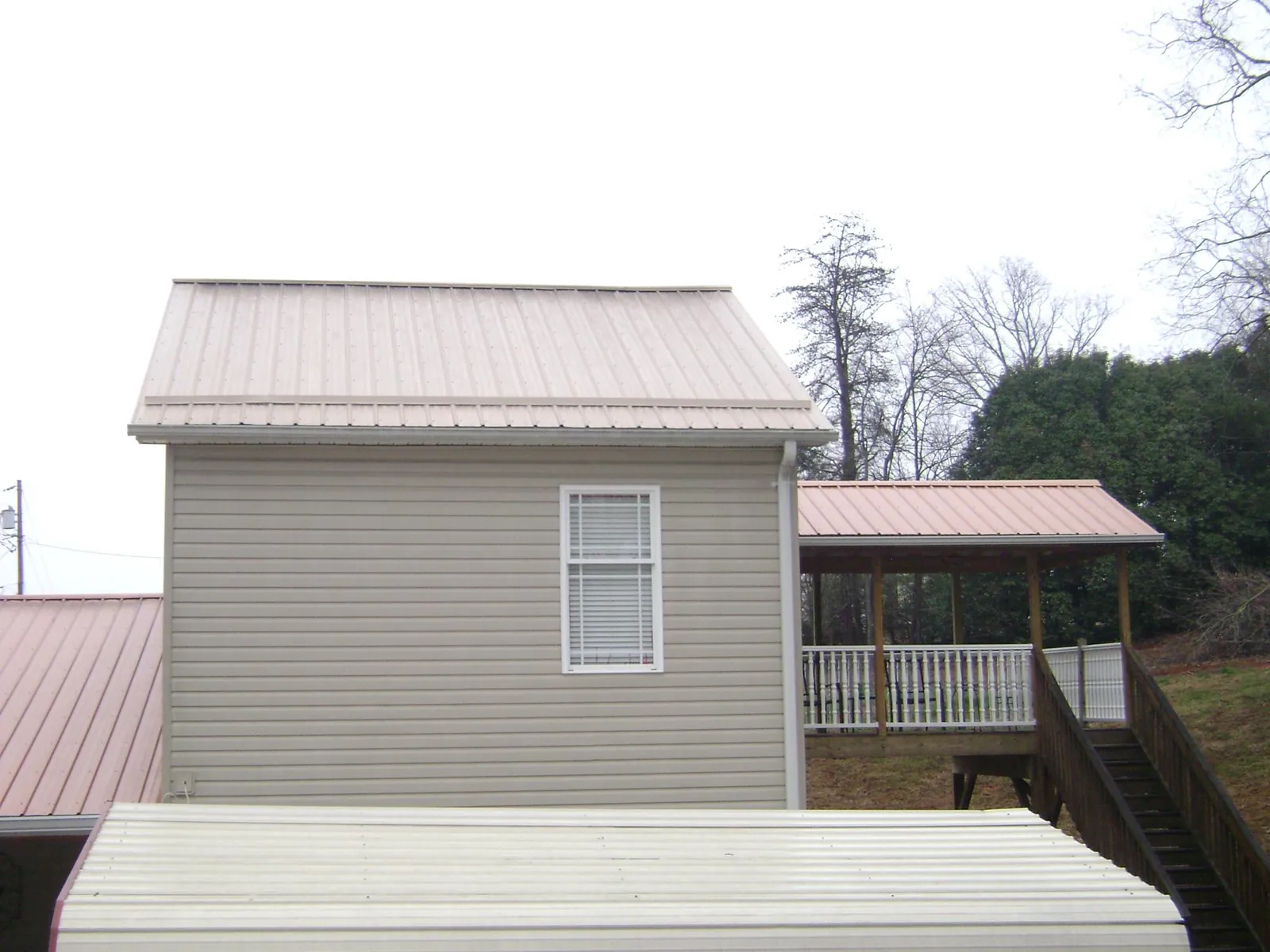 Tan metal roofs on a two story addition and attached porch, from a Roof Replacement job in Middleville
